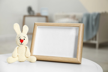 Photo frame and toy bunny on table in baby room interior. Space for text