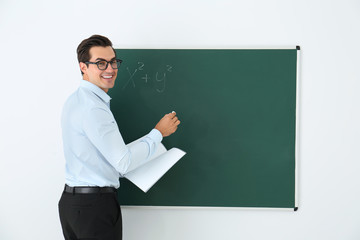 Young teacher with book near blank chalkboard in classroom. Space for text