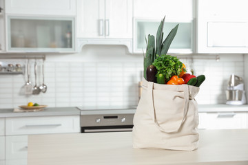 Textile shopping bag full of vegetables on table in kitchen. Space for text