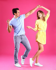 Beautiful young couple dancing on pink background