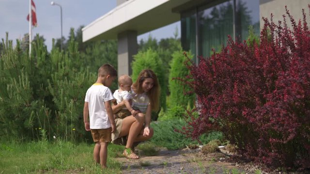 Young mother playing and having fun with her baby boy son brothers in a green garden - Family values warm color summer scene - Green blossoming bushes