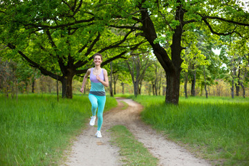 Sports brunette girl jogging in the park. Green forest on the background