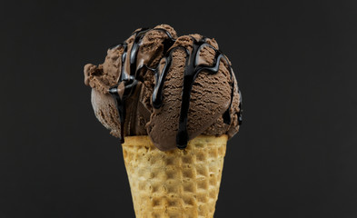 Chocolate ice cream scoop in waffle cone with chocolate sauce isolated black background, Closeup Front view Food concept.