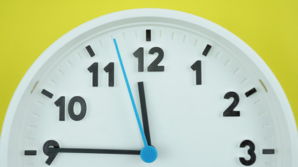 Close up White clock face beginning of time 11.45 on Yellows background, Time concept..