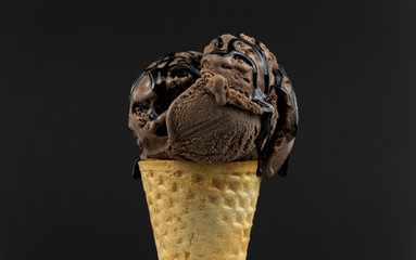 Chocolate ice cream scoop in waffle cone with chocolate sauce isolated black background, Closeup Front view Food concept..