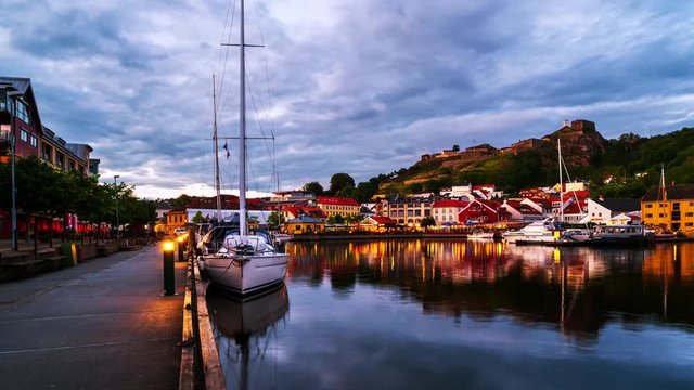 Halden, Norway. View of the illuminated houses and yachts with Fredriksted fortress at the background. Time-lapse at sunset with cloudy sky in summer