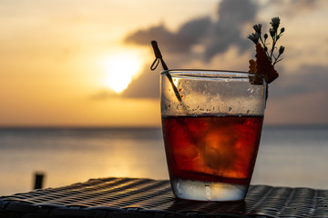 An iced summer cocktail isolated in front of a sunset over the sea