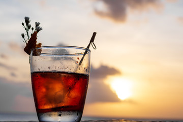 An iced summer cocktail isolated in front of a sunset over the sea