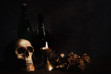 still life of humen skull on table with a glass of wine and wine bottle in a dim light room