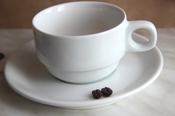 one white classic Cup and two of roasted coffee beans on the saucer, selective focus