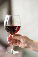 Female hand holding glass with wine on blurred natural background. Space for text. Wine tasting, restaurant, wine tour. Concept alcoholic drinks. 