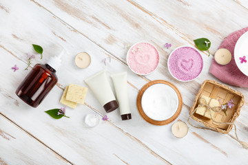 Spa and bath cosmetics with lilac flowers. Bath salt, soap, cream, oil, serum and towel rolls on wooden rustic background. Organic natural cosmetic. Fresh care of body. Banner with copy space top view