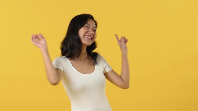Energetic happy young Asian woman smiling and dancing against yellow background