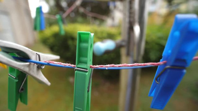 Colorful laundry Pegs clothes pins hanging on washing line outdoors. Windy day in Slow motion