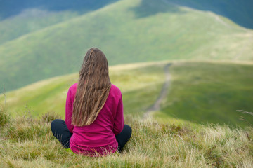 Young tourist, hiker sitting on the top of the hill of mountains and looking at beautiful landscape.