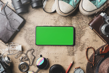 Fototapeta na wymiar Green Screen on Smartphone, Travel Concept Background. Overhead View of Traveler's Accessories on Old Vintage Map