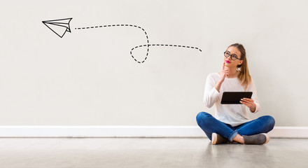 Paper airplane with young woman holding a tablet computer