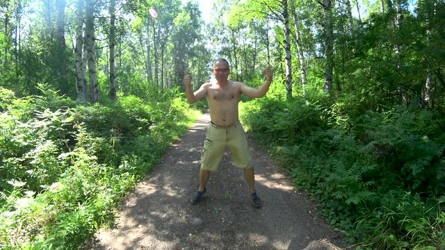 A man in the woods on the trail. Happily jumping and dancing. Shirtless. In cargo shorts. Glasses. Summer.