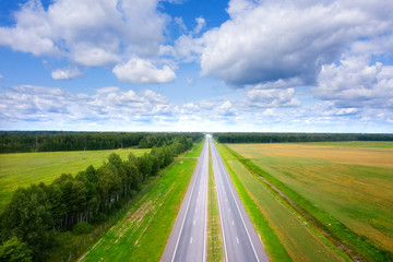 Fototapeta premium Aerial view of road on sunny summer day. Empty Highway from above. Beautiful landscape of road between green meadow and blue sky with clouds