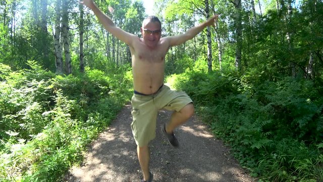 A man in the woods on the trail. Happily running to the meeting. Shirtless. In cargo shorts. Summer. Close-up.