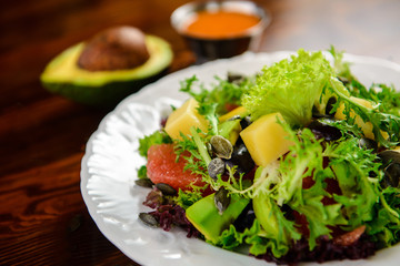 Fresh vegetable salad with avocado, grapefruit and pumpkin seeds on a wooden table in a restaurant