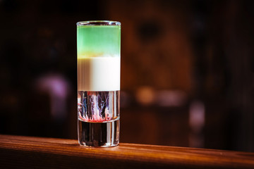 Short drink cocktail in layers with different types of alcohol. Alcoholic drink on a wooden bar counter in a restaurant