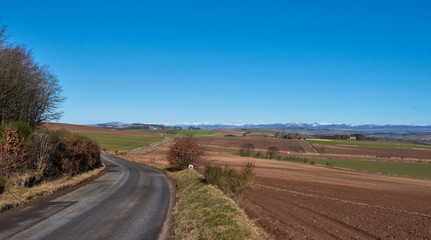 Fototapeta na wymiar A curving minor road near Letham in Angus, wends its way towards a crossroads with a magnificent view of the snow capped Angus Glens beyond.
