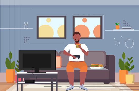 Fat Obese Man Sitting On Couch Eating Hamburger Using Joystick Game Pad Overweight Guy Plying Video Games On Tv Unhealthy Lifestyle Concept Living Room Interior Flat Horizontal Full Length