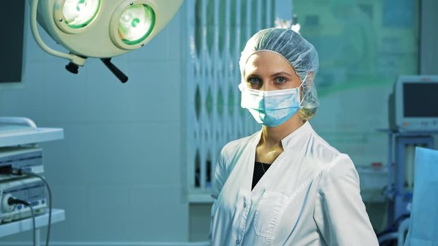 Portrait of a surgeon doctor, after surgery. A tired female surgeon looks into the camera and takes off a surgical mask, she smiles