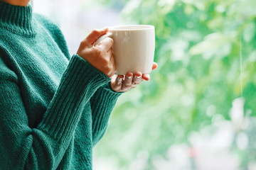 Women wearing green sweaters in their hands holding a white coffee cup in a relaxed mood at the coffee shop