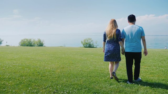 Young multi-ethnic couple walking along green meadows, go forward where beautiful clouds are on the horizon