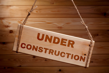 Wooden signboard with the words UNDER CONSTRUCTION on a rough rope on a beautiful wooden background
