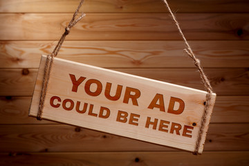 Wooden signboard with the words your ad could be here on a rough rope on a beautiful wooden background