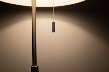 Pull cord switch of a lamp with warm light against white wall. Concept of home, quiet and night...