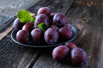 Fototapeta na wymiar Fresh violet plums at dark wooden table background