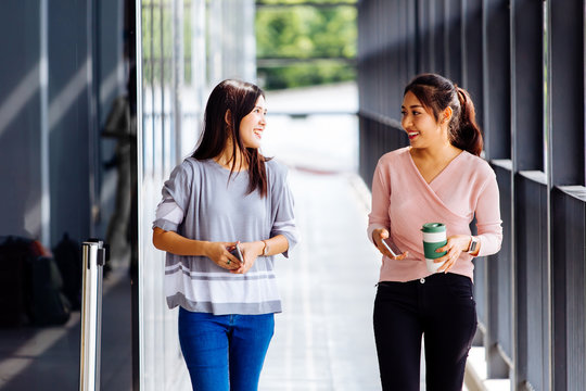 Young Asian business women talking while walking in office building in casual wear. Two girls strolling and discussing outdoors