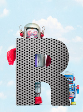 retro robots holding a big  metal letter  R with blue sky