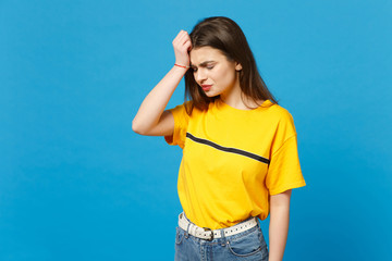 Portrait of displeased crying young woman in vivid casual clothes keeping eyes closed, putting hand on head isolated on bright blue background in studio. People lifestyle concept. Mock up copy space.