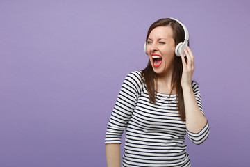 Young brunette woman girl in casual striped clothes posing isolated on violet purple background studio portrait. People sincere emotions lifestyle concept Mock up copy space Listen music in headphones