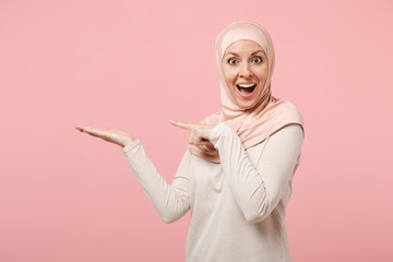 Surprised arabian muslim woman in hijab light clothes posing isolated on pink background in studio....