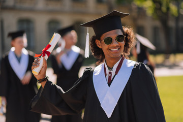 Cheerful graduant raising hand with his diploma.