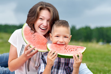 Mother and son eating watermelon in meadow or park. Happy family on picnic. outdoor portrait