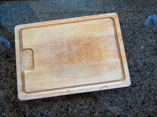 Isolated large wooden cutting board on a granite kitchen counter 