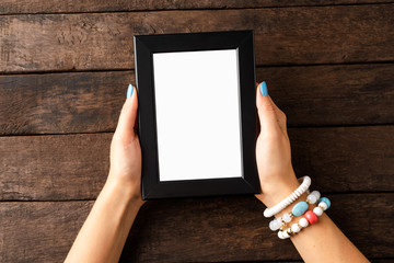 Woman’s hand holding empty photo frame on wooden table. Top view