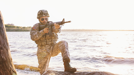 Soldier in camouflage taking aim near river