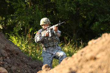 Soldier in camouflage taking aim outdoors