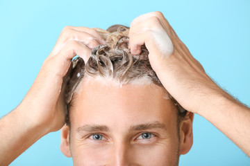 Fototapeta premium Handsome young man washing hair against color background, closeup