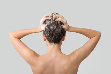 Beautiful young woman washing hair against grey background, back view