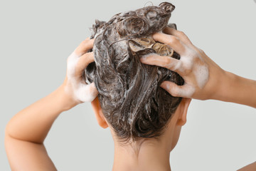 Beautiful young woman washing hair against grey background, back view