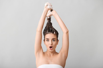 Funny young woman washing hair against grey background